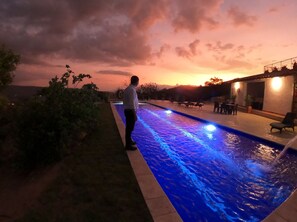 A swimming pool with a person standing by the edge, surrounded by a patio area with outdoor seating and a building in the background. - Hotel Boutique Feria Internacional  (Bogotá)