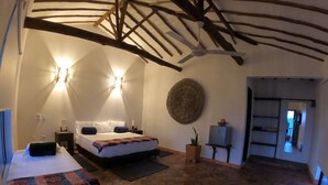 A room with two beds, a ceiling fan, a wall-mounted lamp, a potted plant, and a wooden floor.