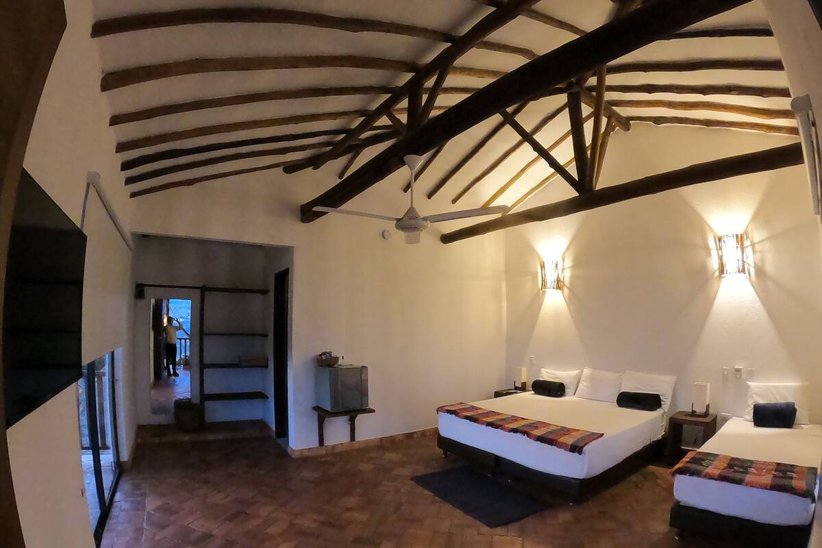 A room with two beds, a wooden ceiling, and a small table.