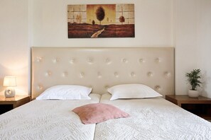 Een net opgemaakt bed met hoofdbord, twee kussens, een bedlampje en een schilderij aan de muur.
