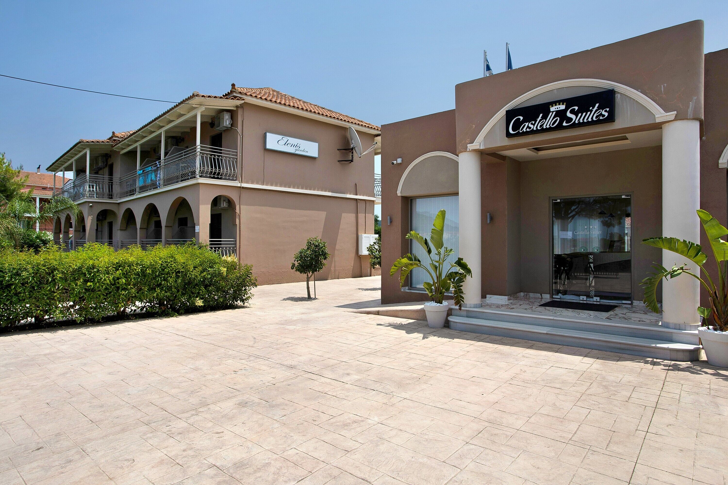 A hotel with a sign reading 'Castello Suites,' featuring a balcony with railings and a tiled roof.