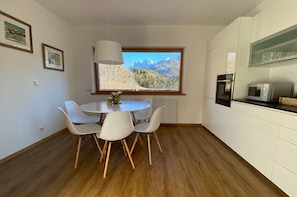A modern kitchen with white cabinets, a dining table with chairs, a window with a mountain view, and built-in appliances.