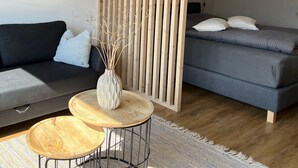 Ett modernt vardagsrum med en mörk soffa, ett litet träbord, en dekorativ vas och en grå soffa med kuddar.