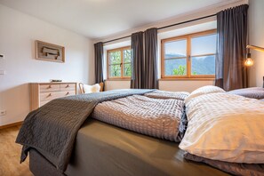 Une chambre à coucher avec un lit, une commode, une fenêtre avec des rideaux et un tableau accroché au mur.
