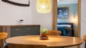 Ett runt träbord med en krukväxt, en hängande, flätad lampa och ett träskåp i bakgrunden.
