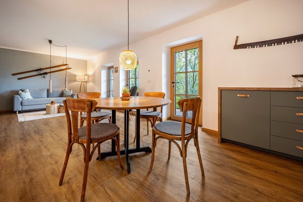 Un coin repas comprenant une table ronde, quatre chaises, un luminaire suspendu, un canapé et un meuble de rangement.