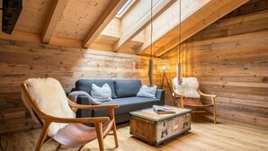 Interior acogedor de una cabaña de madera con un sofá, dos sillones, una mesita y una lámpara.