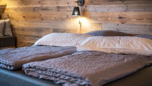 Una cama con una manta texturizada, almohadas y una lámpara de pared.