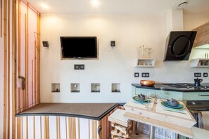 Una cocina moderna con televisión de pantalla plana, horno integrado y comedor con mesa y sillas de madera.