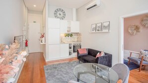 Uma sala de estar moderna com um sofá, uma mesa de centro de vidro e uma área de cozinha com um relógio e obras de arte na parede.