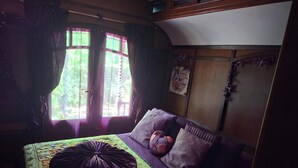 A bedroom with a bed, purple bedding, a window with curtains, and a wooden wardrobe.