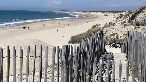 A beach with a wooden fence, a bicycle, and a sandy shore.