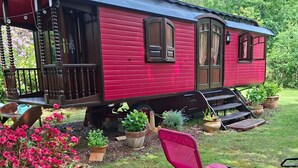 A red mobile home with a porch, steps, and potted plants.