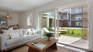 A modern living room with a sofa, coffee table, and a view of a balcony with outdoor furniture. - Apartment "Luxury Boho Style Nazaré" with Sea View, Shared Pool & Wi-Fi (Nazaré)