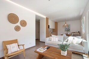 Un soggiorno moderno con un divano, un tavolino in legno e una poltrona in vimini. Si notano decorazioni murali tessute e un lampadario.