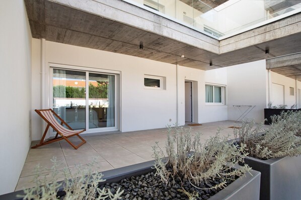 A modern outdoor patio area with a lounge chair, potted plants, and a concrete ceiling.