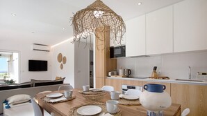 A modern kitchen with white cabinets, a wooden dining table set with plates, cups, and a decorative vase. - Apartment "Luxury Boho Style Nazaré" with Sea View, Shared Pool & Wi-Fi (Nazaré)