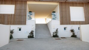 A building entrance with a staircase leading to a covered area, wooden slats on the walls, and potted plants. - Apartment "Luxury Boho Style Nazaré" with Sea View, Shared Pool & Wi-Fi (Nazaré)