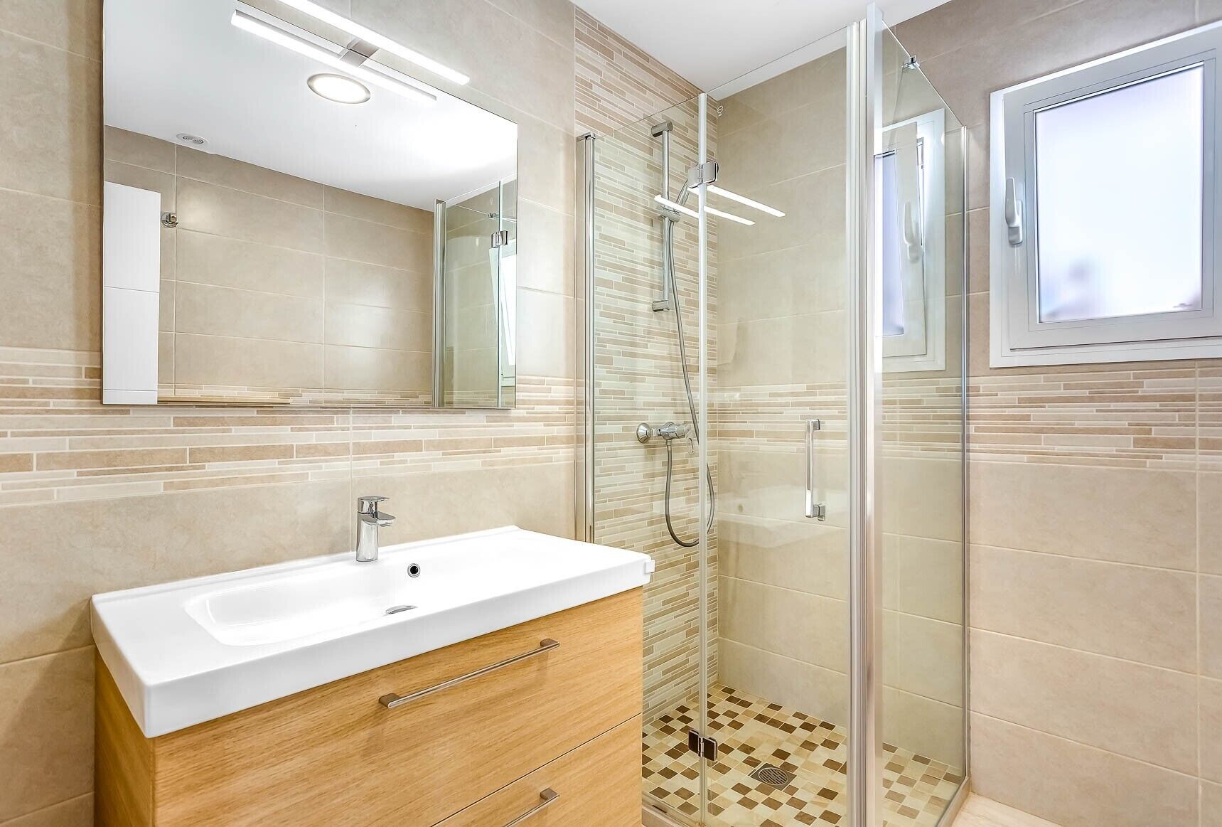 A modern bathroom with a white sink, wooden vanity, glass shower enclosure, and a large mirror.
