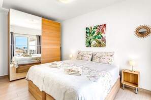 Ein Schlafzimmer mit Bett, Kleiderschrank, Nachttisch, Spiegel und einer Wand mit Pflanzen und Vogelmotiven.
