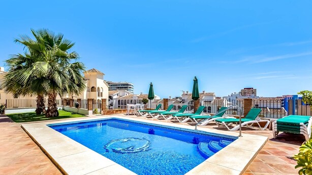 A rectangular swimming pool with a clear blue center, surrounded by lounge chairs and palm trees. - Holiday Apartment 'Torreblanca Deluxe Holiday Home' with Sea View, Shared Pool & Wi-Fi (Fuengirola)