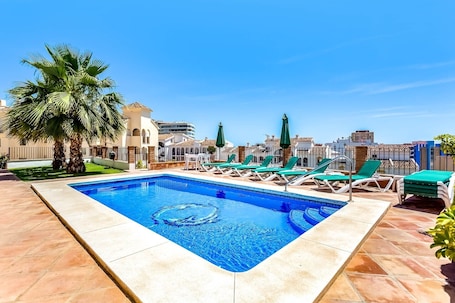 A rectangular pool with clear blue water, surrounded by lounge chairs and palm trees.. Studio Torreblanca close to beach