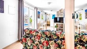 A living room with a sofa, a TV, and a dining area with chairs and a table.