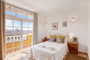 A bedroom with a bed, two nightstands, a window with curtains, and a view of mountains.