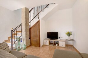 A living room with a staircase, a television, a small table with a plant, and a sofa.