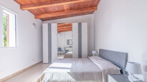 A bedroom with a wooden ceiling, a bed with a grey headboard, a bedside table with a lamp, and a window. - Villa Lorenzo with Private Garden, Whirlpool & Wi-Fi (Avola)