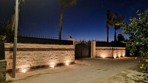 A gated entrance with a stone wall and a metal gate, surrounded by palm trees and a clear night sky. - Villa Lorenzo with Private Garden, Whirlpool & Wi-Fi (Avola)