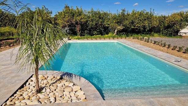 A rectangular swimming pool with clear blue water, surrounded by a stone deck and a small palm tree. - Villa Lorenzo with Private Garden, Whirlpool & Wi-Fi (Avola)