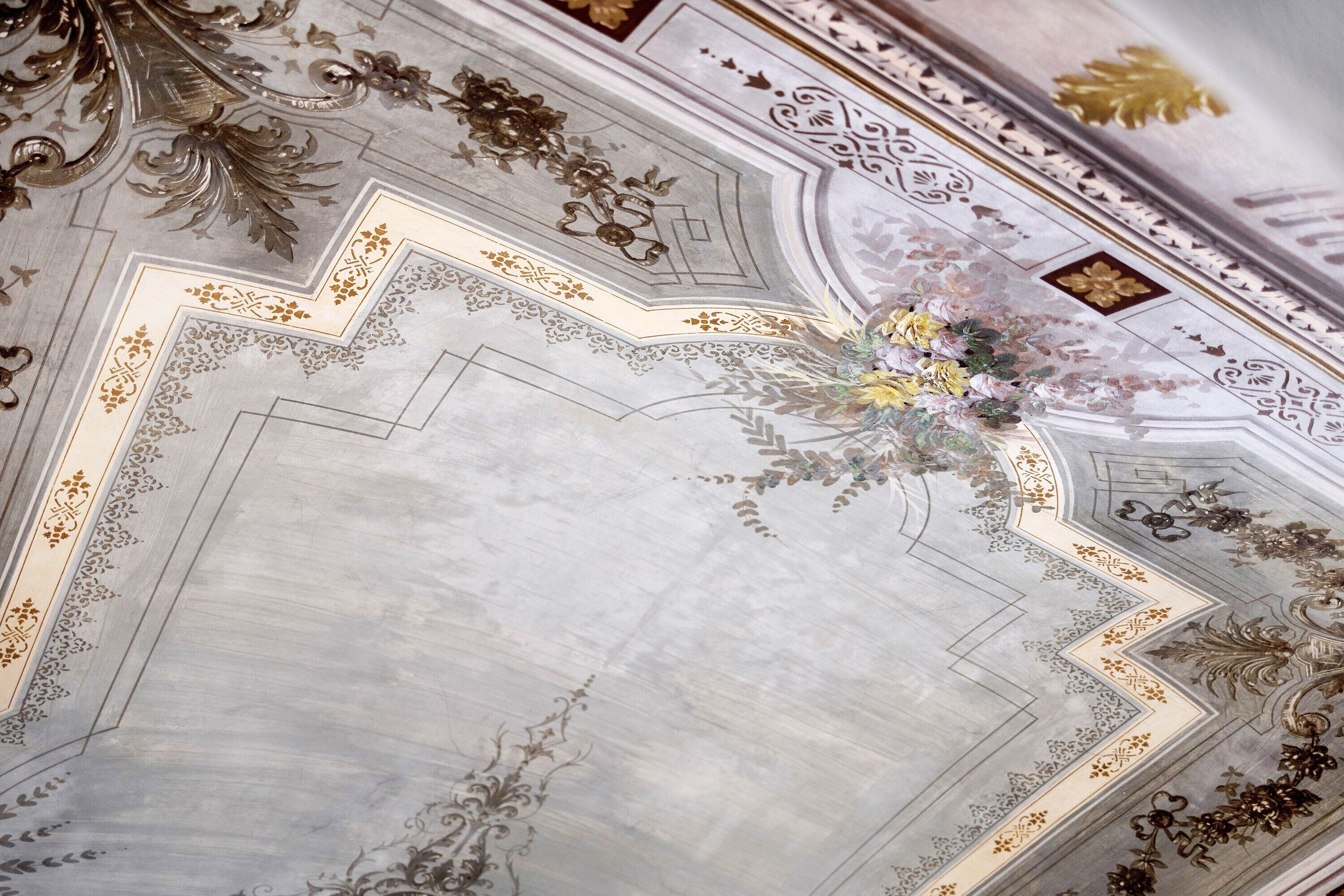 A ceiling with ornate gold and white patterns, a central floral arrangement, and a geometric design.