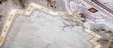 A ceiling with ornate gold and white patterns, a central floral arrangement, and a geometric design.