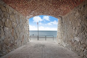 Un arc en pierre qui mène à une plage où se trouve un mât de drapeau.