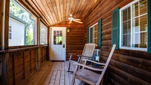 Een houten chalet met veranda, schommelstoelen en een deur met raam.