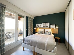 Ein Schlafzimmer mit Bett, Nachttisch, Sessel, kleinem Tisch und Blick auf den Balkon.