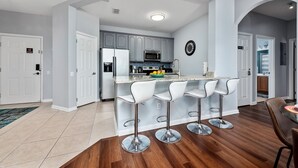 Een moderne keuken met grijze kastjes, een centraal eiland met barkrukken, een magnetron en een klok aan de muur.