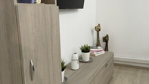 A modern living room with a wooden cabinet, a flat-screen TV mounted on the wall, and a small table with decorative items. - Charming 2-bed Apartment in Kallithea (Kallithea)