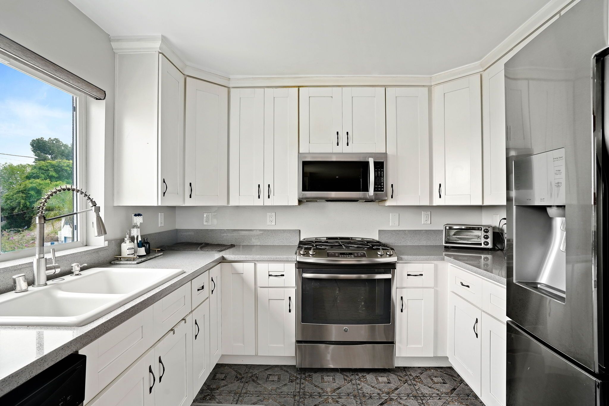 A modern kitchen with white cabinets, a stainless steel refrigerator, a built-in oven, and a microwave.