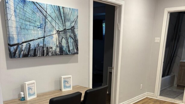 A dining area with a wooden table, two black chairs, and a cityscape painting on the wall.