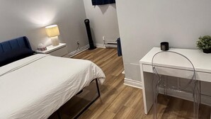 A modern hotel room with a bed, bedside table, lamp, desk, chair, and a small potted plant.