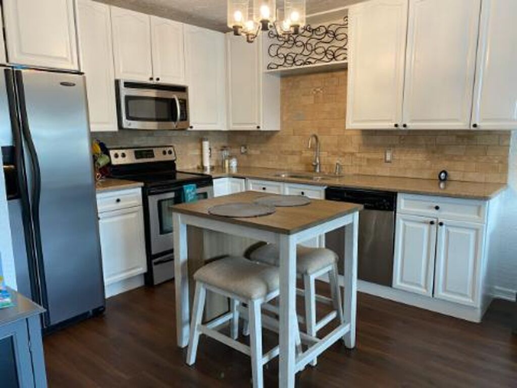 A modern kitchen with white cabinets, stainless steel appliances, and a wooden island with stools.