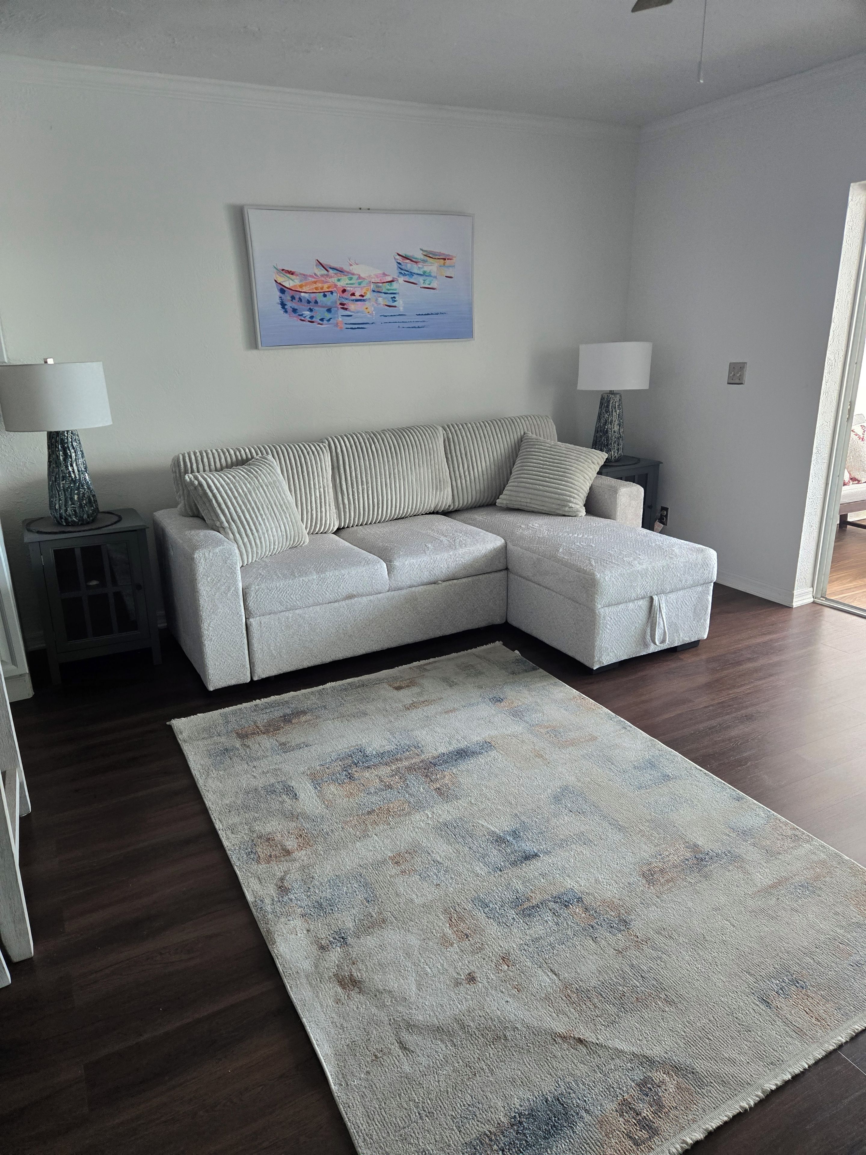 A living room with a grey sectional sofa, a patterned rug, and a painting on the wall.