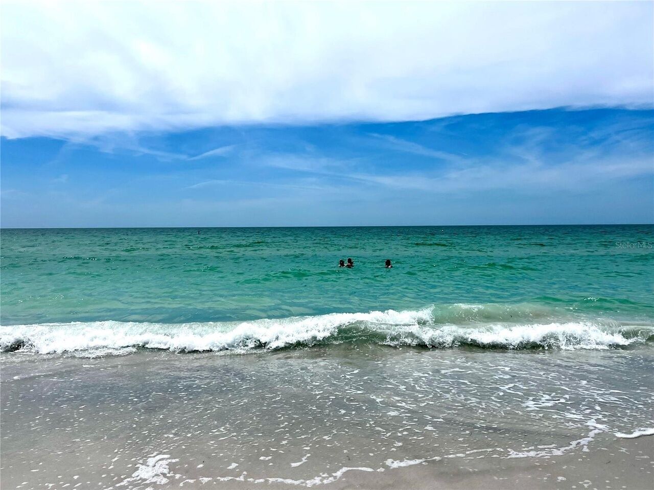 A beach with clear turquoise water and a few people swimming.