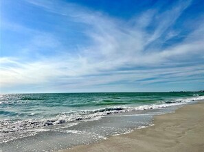 En strand med vågor, en klar himmel och en kustlinje som sträcker sig långt bort.