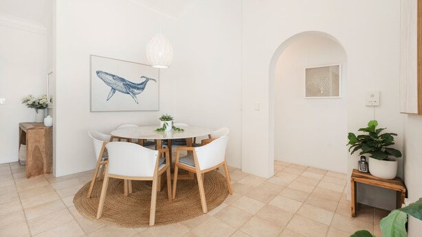 A dining area with a round table, white chairs, a hanging light fixture, and wall art. - Commodore 7 80 Noosa Parade (Noosa Heads)