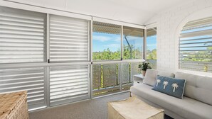 A modern room with large windows, a grey sofa, and a wicker chair. - Commodore 7 80 Noosa Parade (Noosa Heads)