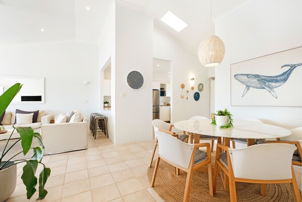 A modern interior with a dining area, a sofa, a kitchen in the background, and a large whale artwork on the wall.