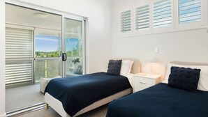 A bedroom with two beds, a nightstand, a lamp, and a sliding glass door leading to a balcony. - Commodore 7 80 Noosa Parade (Noosa Heads)